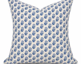 Op de afbeelding: Een vierkant sierkussen met een gebroken witte basiskleur en een herhalend patroon van kleine, blauwe bloemmotieven die in verticale kolommen over het gehele oppervlak van de stof zijn gerangschikt voor een consistent en uniform ontwerp.