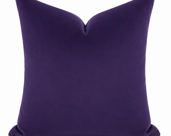 May include: A square throw pillow featuring a solid deep purple velvet fabric cover. The pillow has a distinct karate-chop indentation at the top center, creating two symmetrical peaks on the left and right sides of the top edge.