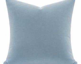 May include: A square throw pillow featuring a solid light blue velvet fabric cover. The pillow has a smooth, uniform texture and a clean, simple design with sharp corners and a soft, plush appearance, presented against a plain white background.
