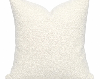 May include: A square throw cushion featuring a textured, off-white bouclé fabric cover. The surface of the cushion has a distinct nubby, looped appearance with a consistent cream-coloured tone throughout the entire exterior of the item.