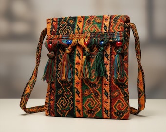 May include: A rectangular crossbody bag with a woven, patterned design in orange, green, black, and brown. The bag features colorful tassels and beaded accents. The strap is made of the same woven material.