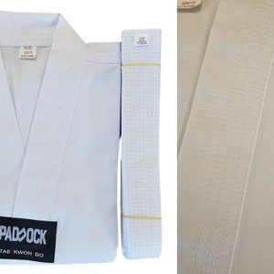 Puede incluir: Uniforme de Taekwondo blanco con un cinturón blanco y un parche negro que dice "PADOCK TAE KWON DO".