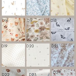 K&ouml;nnte beinhalten: Eine Sammlung von zw&ouml;lf Stoffmustern aus doppeltem Baumwollmull, beschriftet von D13 bis D24, mit verschiedenen Mustern wie Eichh&ouml;rnchen, blauen Blumen, gelben Bl&uuml;ten, Waldtieren, Vintage-Blumen, Orcas, Vichy-Karo und Walen.