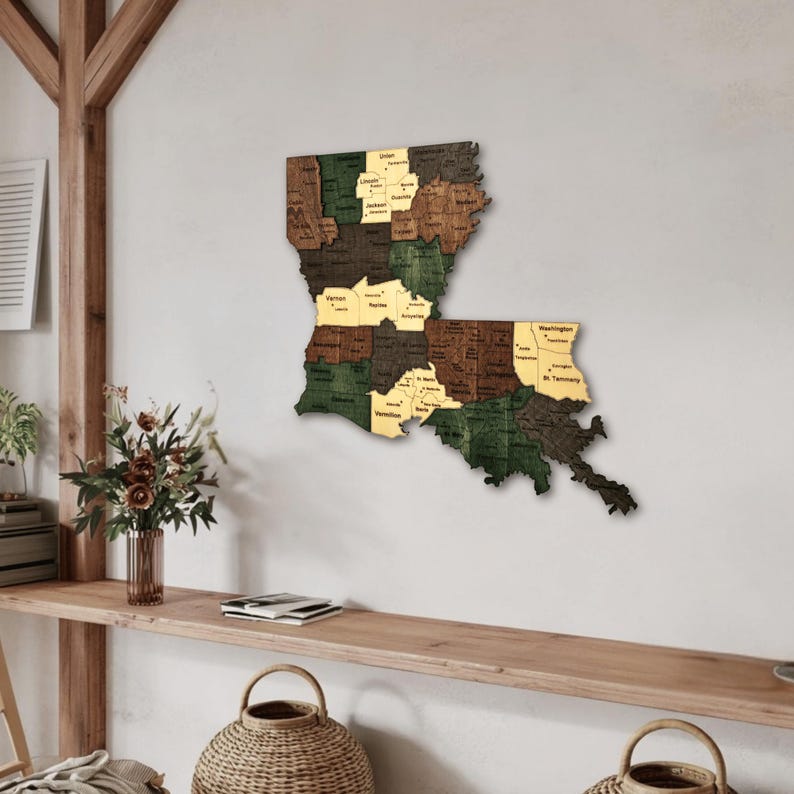 May include: Wooden map of Louisiana, USA, mounted on a white wall. The map is segmented into parishes, each with a different color: brown, green, and tan. The names of the parishes are printed in a small, black font.