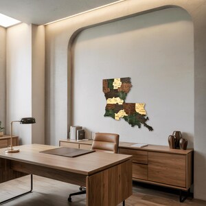 May include: A wooden map of Louisiana, mounted on a wall. The map is segmented into parishes, each with a different wood tone, including green, brown, and gold. The map is displayed in a modern office setting.
