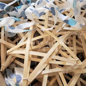May include: A close-up of a pile of unfinished wooden star-shaped frames. The frames are made of thin, light-colored wood and are tied together with string. The frames are surrounded by a blue and white patterned fabric.