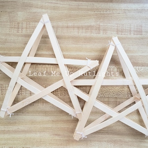 May include: Two wooden star-shaped decorations made from light-colored wooden sticks, joined with white string. The stars are arranged on a light brown wooden surface. The text "Leaf Me Up Hutlights" is visible.