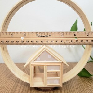 May include: A small wooden house with a white roof and a window. The house is made of popsicle sticks and is sitting on a wooden circle.