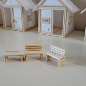 May include: Three miniature wooden benches made of popsicle sticks. The benches are arranged in a row on a white surface.