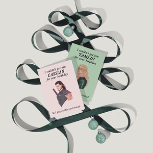 May include: Two greeting cards with illustrations of characters from a fantasy novel. The card on the left features a man with a sword and the text "I couldn't get you Cassian for your birthday. So I got you this card instead." The card on the right features a woman with long blonde hair and the text "I couldn't get you Tamlin for your birthday. So I got you this card instead."