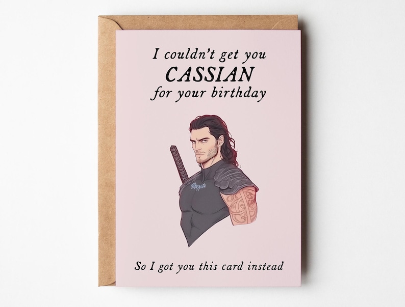 May include: A pink greeting card with a cartoon illustration of a man with dark hair and a sword. The card reads "I couldn't get you CASSIAN for your birthday So I got you this card instead."