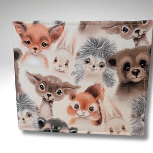 May include: A fabric with a repeating pattern of various woodland animals, including a fox, a deer, a squirrel, a hedgehog, and a rabbit. The animals are depicted in a cartoon style with soft colors and a whimsical feel.