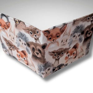 May include: A white fabric wallet with a repeating pattern of cute animal faces. The animals include foxes, deer, squirrels, rabbits, and owls. The wallet is folded closed.