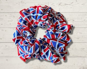 May include: A large scrunchie featuring the Union Jack flag design in red, white, and blue. The fabric is gathered and ruffled, creating a voluminous accessory. The scrunchie is a hair accessory.