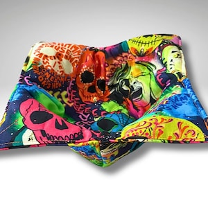 May include: A multi-coloured bowl cosy with a striking skull and face design. The fabric features orange, pink, green, and blue hues, creating a bold pattern. The cosy is designed to hold a bowl of food.