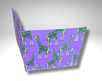 May include: A purple fabric wallet featuring a repeating pattern of giraffes. The giraffes have a yellow outline and dark green spots. The wallet is open, displaying the interior, and is angled to show the pattern.
