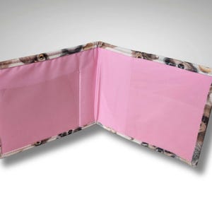 May include: A pink and white wallet with a dog print design. The wallet has two pockets with pink fabric lining.