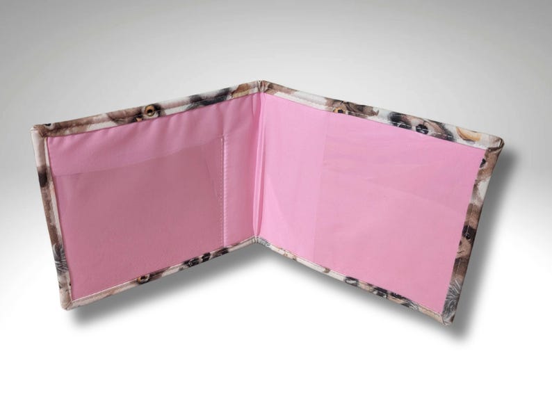 May include: A pink and white wallet with a dog print design. The wallet has two pockets with pink fabric lining.