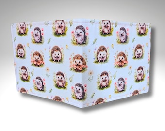 May include: A light blue wallet featuring a repeating pattern of adorable hedgehogs surrounded by flowers. The hedgehogs have brown and black quills and are set against a backdrop of small flowers and green foliage.