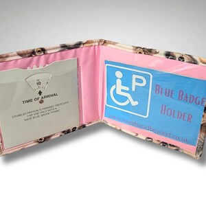 May include: A pink and blue fabric wallet with a clear plastic window for a blue badge. The wallet has a built-in timer for parking and the text "Blue Badge Holder" is printed on the front.