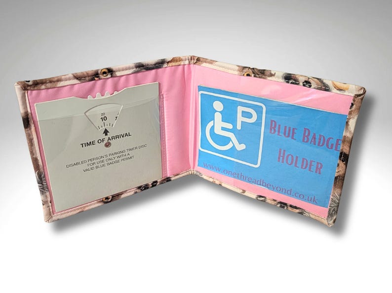 May include: A pink and blue fabric wallet with a clear plastic window for a blue badge. The wallet has a built-in timer for parking and the text "Blue Badge Holder" is printed on the front.