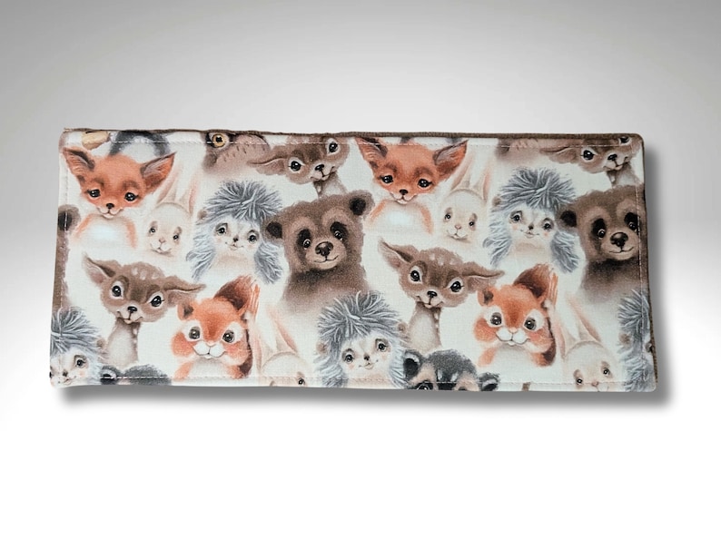 May include: A brown fabric wallet with a white background and a repeating pattern of various woodland animals, including squirrels, foxes, deer, and bears.