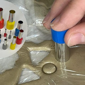 Könnte beinhalten: Eine Sammlung von elektrischen Drahtverbindern in verschiedenen Größen und Farben, darunter Blau, Rot, Gelb und Grau. Eine Hand verwendet einen blauen Verbinder. Diese Verbinder werden für die elektrische Verdrahtung verwendet.
