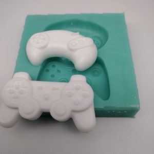 May include: A teal silicone mould with two white plastic moulds of video game controllers. The controllers are in the shape of a classic video game console controller and a modern video game controller.