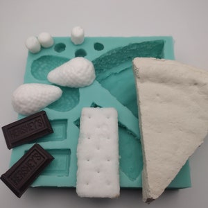 Puede incluir: Un molde de silicona turquesa con varias formas para hacer s'mores. El molde incluye formas para galletas graham, malvaviscos y barras de chocolate. El molde está lleno de fondant blanco y marrón.