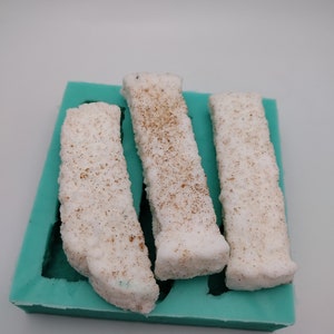 May include: Three white rectangular bars with a speckled texture are in a teal silicone mold.