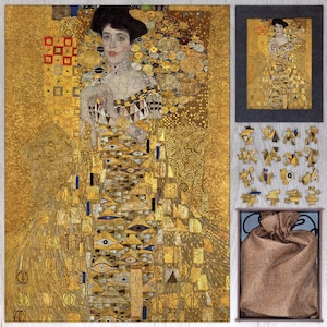 Puede incluir: Un rompecabezas de madera con una pintura de una mujer con un vestido dorado con un patrón geométrico. El rompecabezas está en una caja con una bolsa de arpillera y una versión más pequeña de la imagen del rompecabezas.