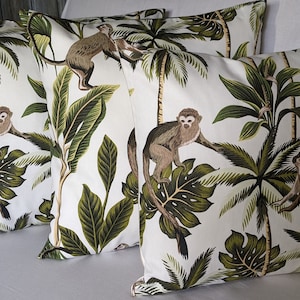 May include: Four white cushion covers with a tropical print featuring monkeys, palm trees and green leaves.