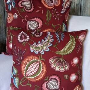 May include: Two red throw cushions with a floral pattern. The cushions feature a repeating design of stylised flowers, leaves, and hearts in shades of pink, green, blue, and white.