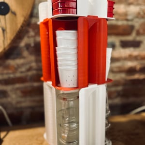 Peut inclure: Un distributeur en plastique blanc et rouge avec plusieurs compartiments pour contenir des tasses et des bols. Le distributeur est empilé avec des tasses blanches et des bols rouges.