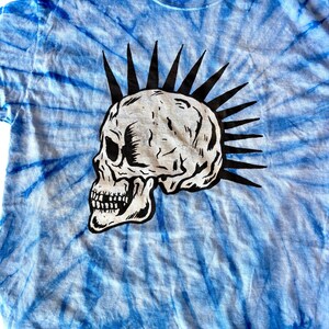 May include: A blue tie-dye t-shirt with a black and white skull graphic. The skull has a mohawk.