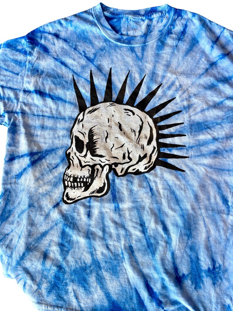 May include: A blue tie-dye t-shirt with a black and white skull graphic. The skull has a mohawk.