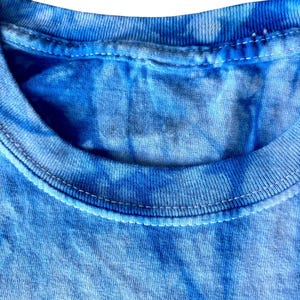 May include: Close-up of the neckline of a blue tie-dye t-shirt. The fabric is soft and has a subtle, faded look.