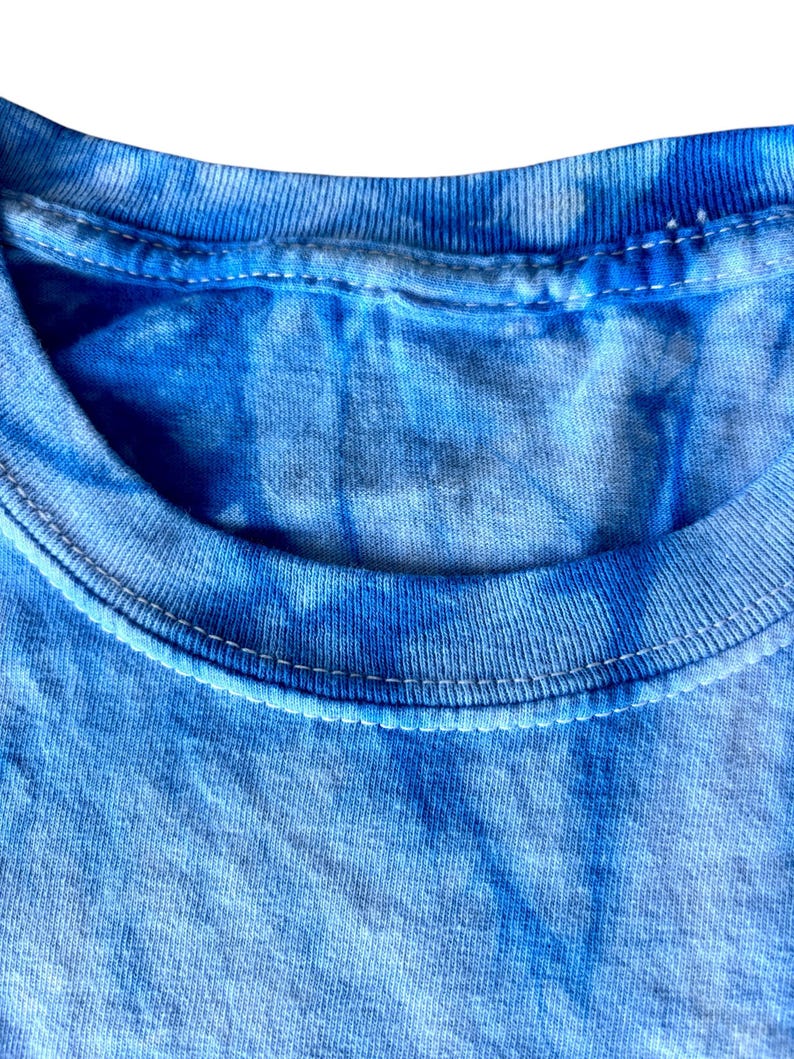May include: Close-up of the neckline of a blue tie-dye t-shirt. The fabric is soft and has a subtle, faded look.