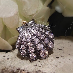 May include: A black and silver seashell pendant with clear rhinestones. The pendant is on a white background.