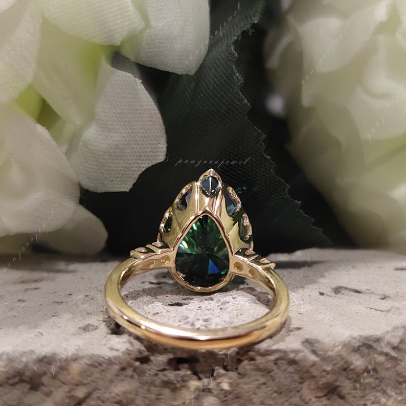 May include: A gold ring with a pear-shaped green gemstone surrounded by smaller gemstones. The ring is set with a halo of smaller gemstones.