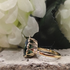 May include: A gold ring with a large, green gemstone set in a heart-shaped halo. The ring is accented with smaller diamonds on the band.