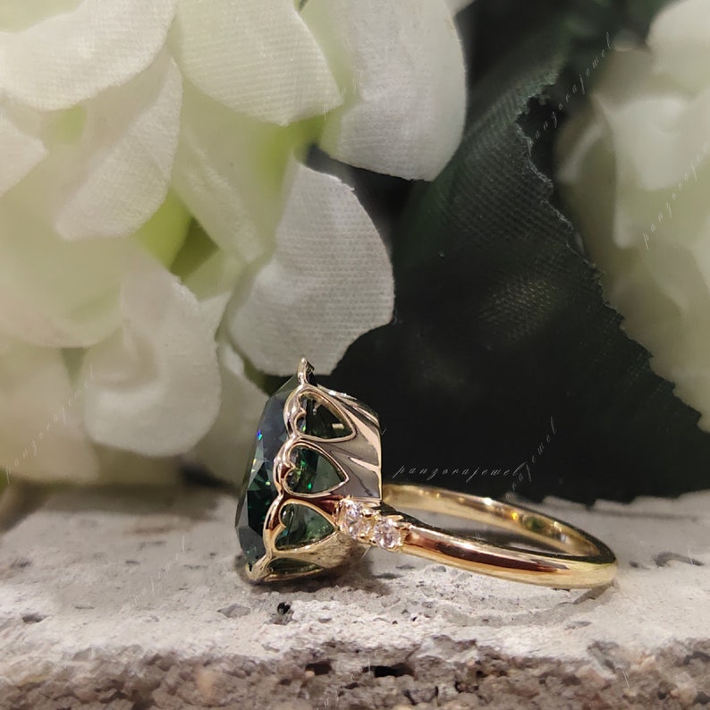 May include: A gold ring with a large, green gemstone set in a heart-shaped halo. The ring is accented with smaller diamonds on the band.