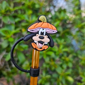 May include: A brown and orange Goofy character straw topper with a black and orange hat. The straw topper is attached to a clear plastic straw with a black ring.