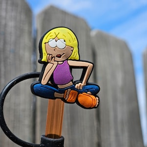 May include: A yellow, orange, blue, and purple cartoon character with blonde hair is sitting on a brown straw with a black ring around it. The character is wearing a purple tank top and blue jeans. The character is sitting with their legs crossed and their hands on their knees. The character is looking to the right.