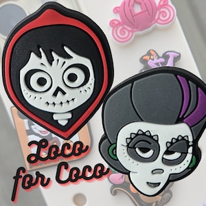 May include: Two colorful, cartoon-style, skull-shaped figures with black hair and red and purple accents. The text "Loco for Coco" is written in white letters on a black background.