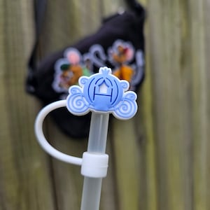 Puede incluir: Un adorno para pajita de plástico azul y blanco en forma de carroza de Cenicienta. El adorno está unido a una pajita de plástico transparente.