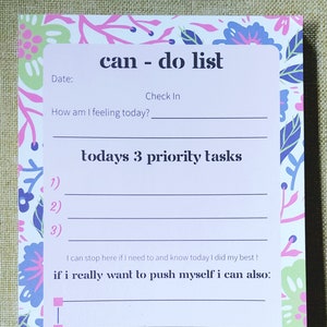 May include: A floral patterned notepad with the words "can - do list" at the top. The notepad includes sections for a date, a check-in, and today's 3 priority tasks. The notepad has a light pink background with a floral design.