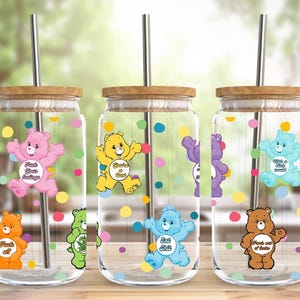 Puede incluir: Tres tarros de vidrio con tapas y pajitas, cada uno con un personaje de Care Bear diferente con un lema. Los tarros están decorados con lunares de colores. Los lemas son "Compartir y cuidar", "Alegrar y compartir", y "Desear un pequeño deseo".