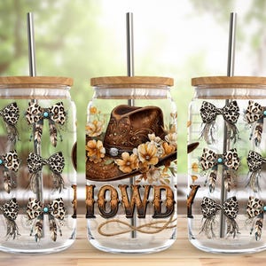 May include: Three clear glass mason jars with wooden lids and metal straws. Each jar has a different design. One jar has a brown cowboy hat with flowers and the word "HOWDY" on it. The other two jars have a pattern of brown and white leopard print bows with turquoise accents.