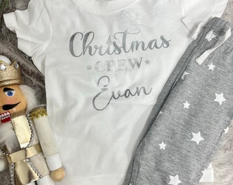 May include: White t-shirt with silver glitter text that says "Christmas Crew Evan" and gray sweatpants with white stars.